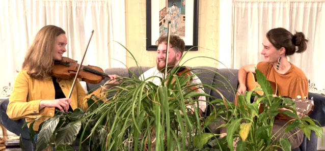 The Baby Corns playing on a couch in front of lush plants